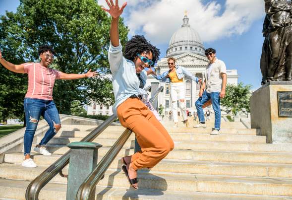A Black woman slides down a railing with joy as three friends around her cheer in front of the Capitol building