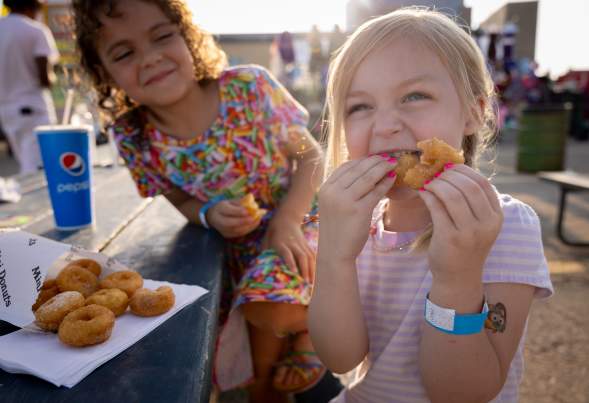 Two young girls eating miniature donuts at a pumpkin patch