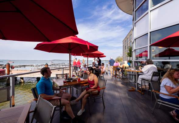 A couple sits at a table on the patio of The Boathouse at The Edgewater. The patio is alongside Lake Mendota