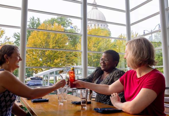 Three people cheers with cocktails in hand at Graze with views of the State Capitol Building