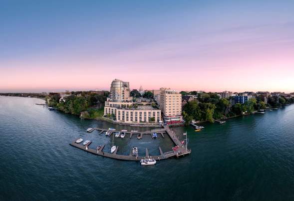 A wide view of the Edgewater Hotel on Lake Mendota with a sunset of pinks and purples in the background.