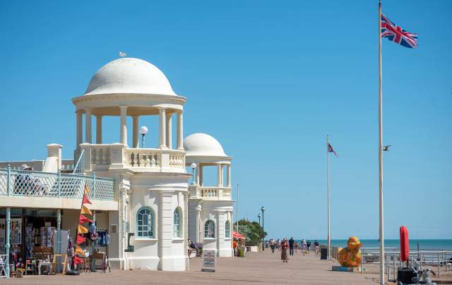A sunny day in Bexhill on the promenade, with white cafe buildings and shops