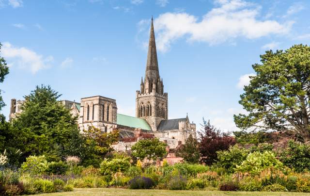 A view of Chichester Cathedral from the gardens with the spire reaching blue sky