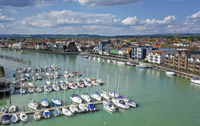 Yachts moored on the river at Littlehampton harbour, with riverside apartments on the opposite side