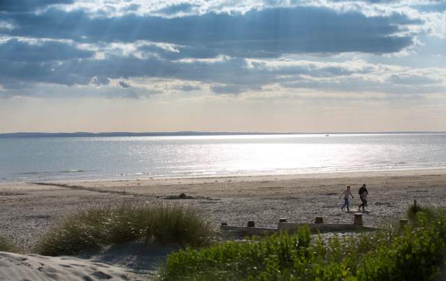 Sunny day at West Wittering beach looking out to sea, with a couple walking in the sandy dunes