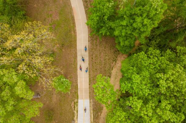 Aerial view of cyclists riding the A Street Flyover, a paved trail surrounded by lush green trees in Bentonville, Arkansas.
