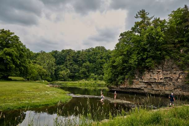Three people fishing in a stream next to a bluff in a state park.