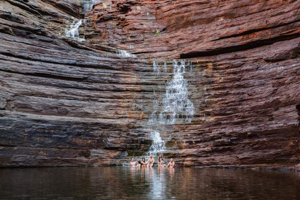 A group sitting at the base of the Joffre Gorge waterfall, with reflections in the pool in front of them.