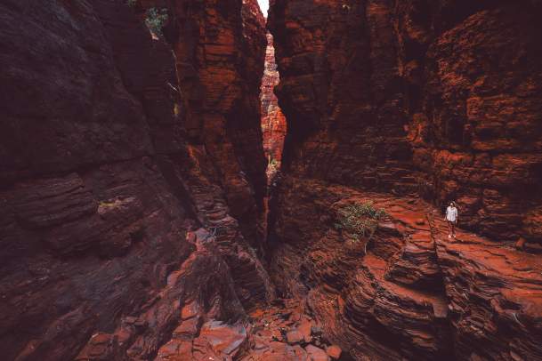 Woman walking through Knox Gorge in Karijini National Park, with towering red rock gorge walls