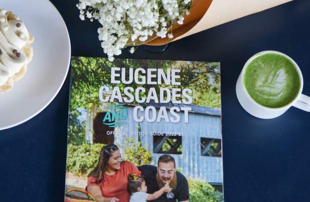 A visitor guide sits on a blue table with a matcha latte, a pastry and a small bouquet of flowers.