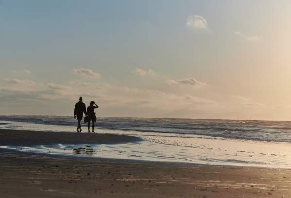 A silhouetted couple walks along the beach