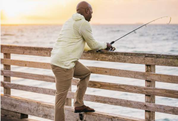 Man fishing on a pier wearing khaki pants and a long sleeve light green fishing shirt