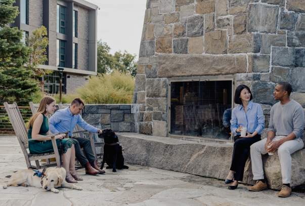 Four people and two guide dogs sit together chatting at a firepit.