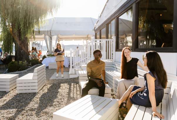 A group of people sit together sharing a laugh on the patio of The Sailhouse.