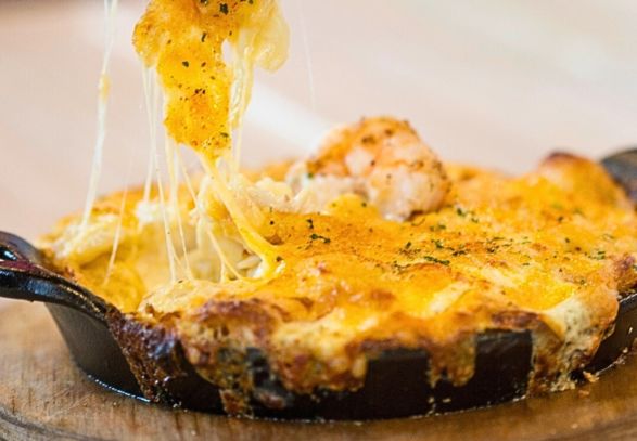 Seafood dip with a cheddar cheese pull of creamy seafood from a black cast iron pan.