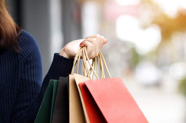 Picture on a persons hand holding shopping bags with a blurry street view in the background.