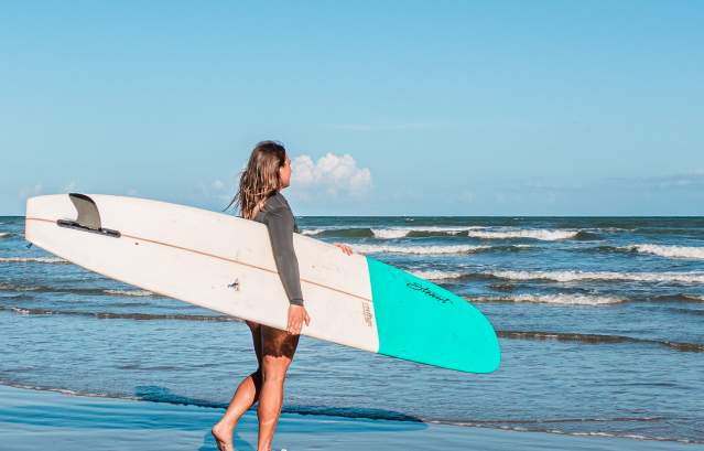 Girl holding a white and blue surf board walking into the water.