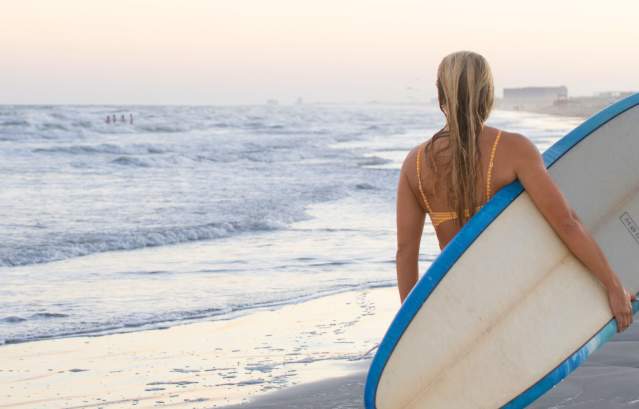 A girl carrying a surfboard on her side down the beach..