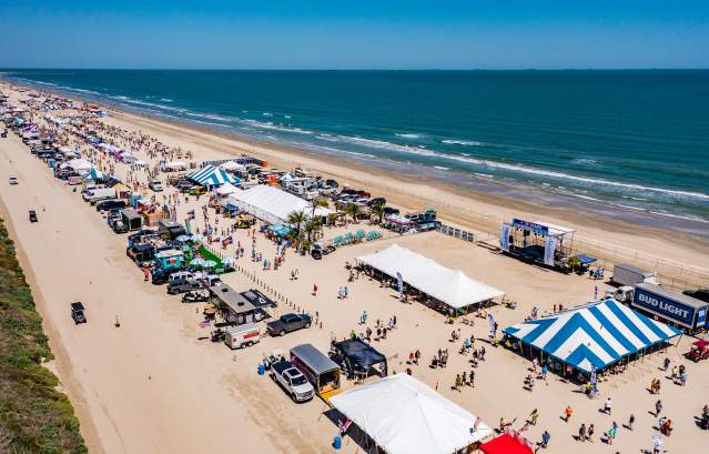 Aerial shot of a long stretch of beach covered in tents and people during a festival.