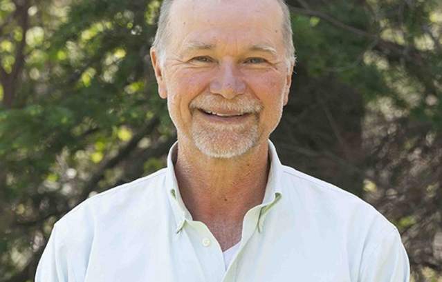 Headshot of a smiling man in front of a blurred forest background