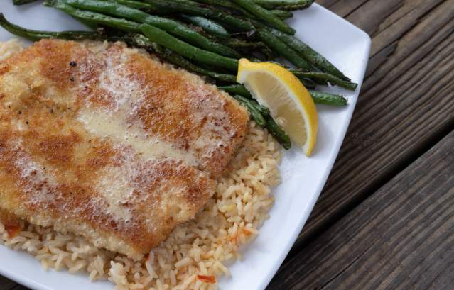 A plate of fried fish with green beans and a lemon sits on a wooden tabletop