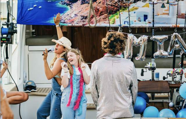 Two people dressed in costume sing into toy microphones aboard a fishing boat