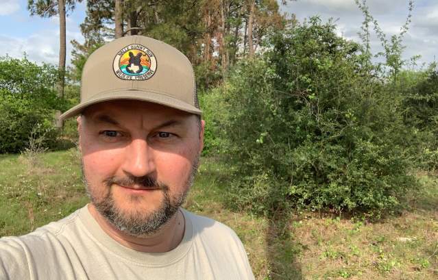 Selfie of a man wearing a hat in front of a natural green setting