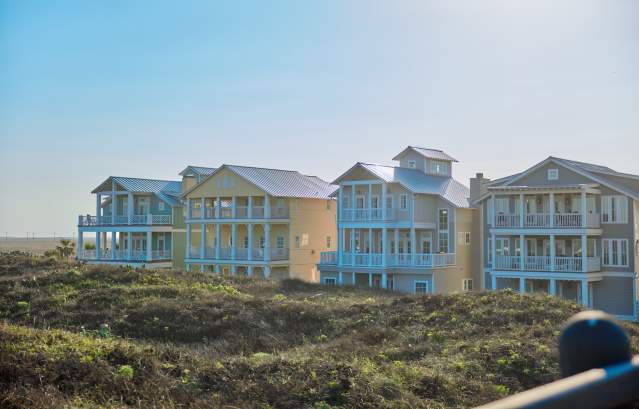 row of 4 large beach houses nestled in dunes in bright sunlight