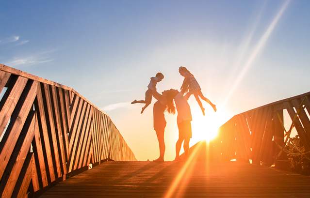 Parents lift their two children in the air on a boardwalk at sunrise in Port Aransas. Texas