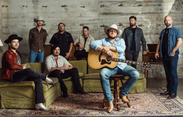 Josh Abbott Band members posing together in a rustic room with instruments and vintage decor.