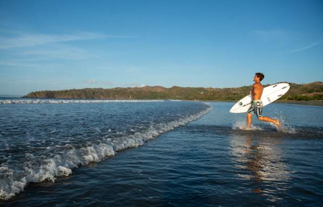 Un hombre con tabla de surf corriendo hacia la playa de Venao, provincia de Los Santos, Panamá