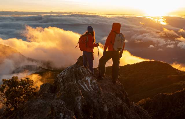Hikers watching the sunrise from the summit of Volcan Baru, surrounded by clouds and mountainous landscapes in Panamá.