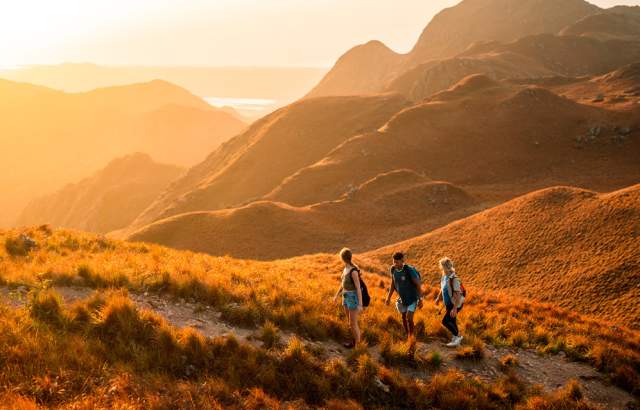 A squad of friends conquering a mountain over a beautiful orange sunset.