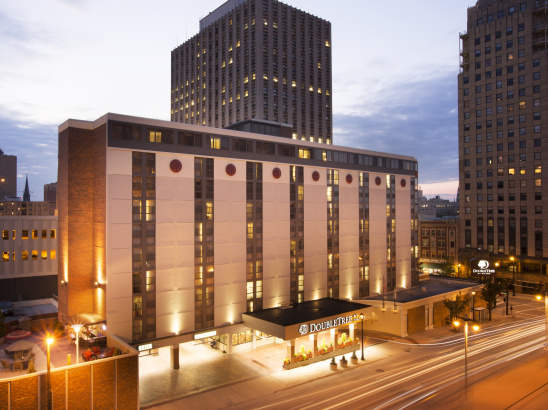 The DoubleTree by Hilton Hotel illuminated by lights against a dimly lit sky, with buildings in the background.