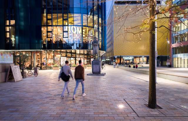 2 people walking in a square in front of HOME venue.