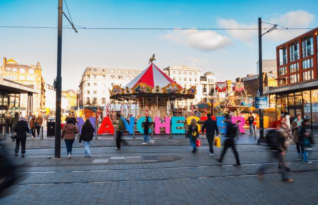 Manchester Christmas Markets with busy stalls and the letters MANCHESTER in the background