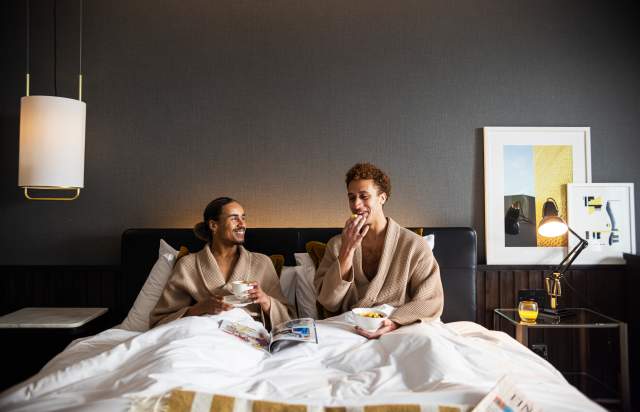 Couple in hotel bed in dressing gowns eating breakfast and drinking coffee