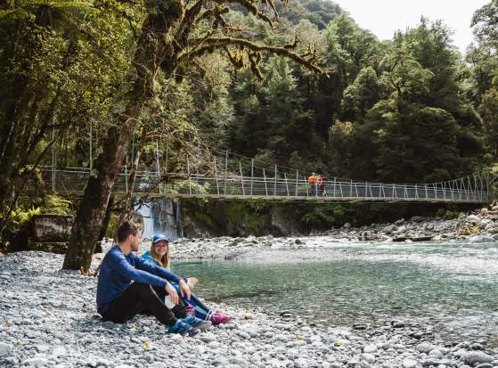 Two people sitting next of a river surrounded by bush