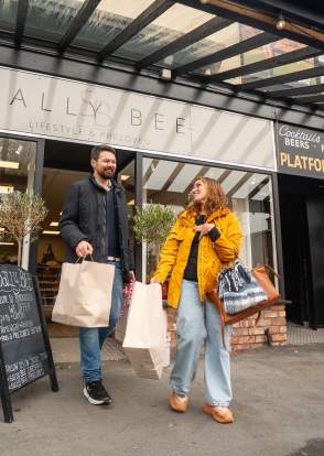 A couple leave a lifestyle shop carrying shopping bags.