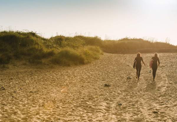 Two ladies walking across the beach with surfboards