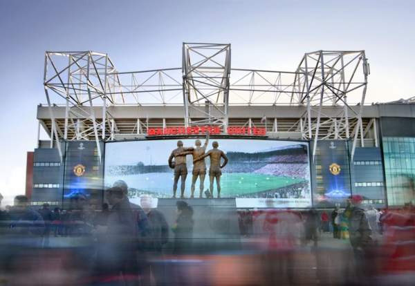 Manchester United football ground with statues and people moving across the front