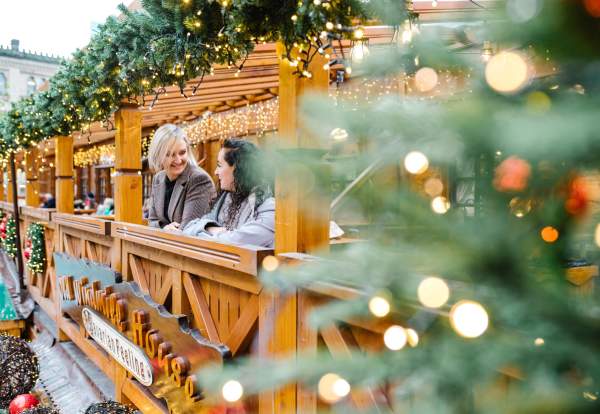 2 people stood on balcony of Christmas Markets with out of focus christmas tree in the foreground