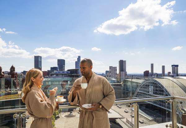 Couple in dressing gowns drinking coffee on Hotel Balcony overlooking Manchester