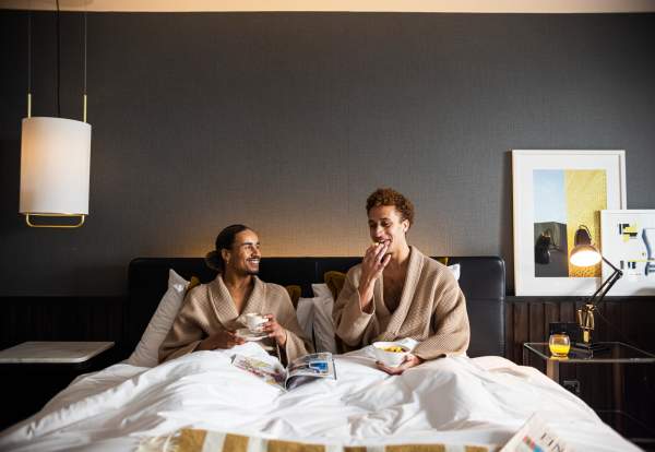 Couple in hotel bed in dressing gowns eating breakfast and drinking coffee
