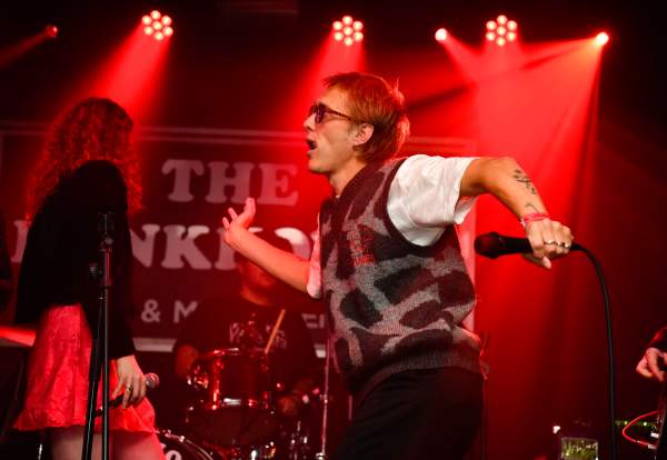 A male singer on a stage wearing sunglasses, holding a microphone, dancing
