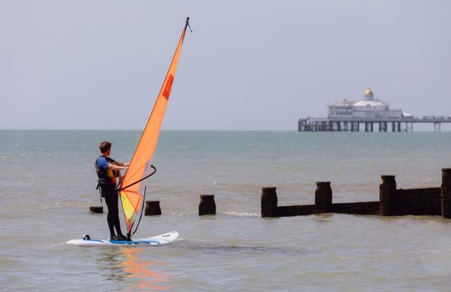 Windsurfer with orange sail looking at the pier on the Sussex coast