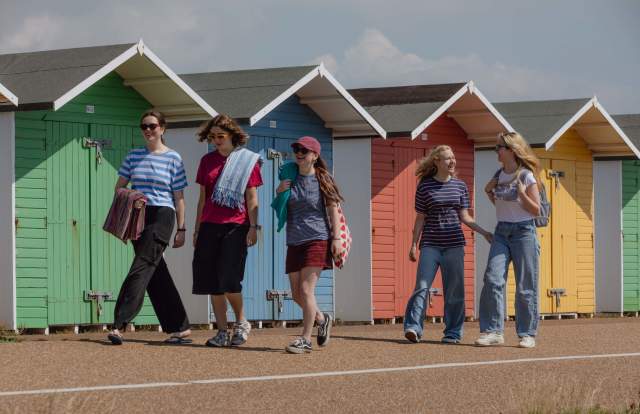 A group walking in front of multi colour beach huts in Sussex