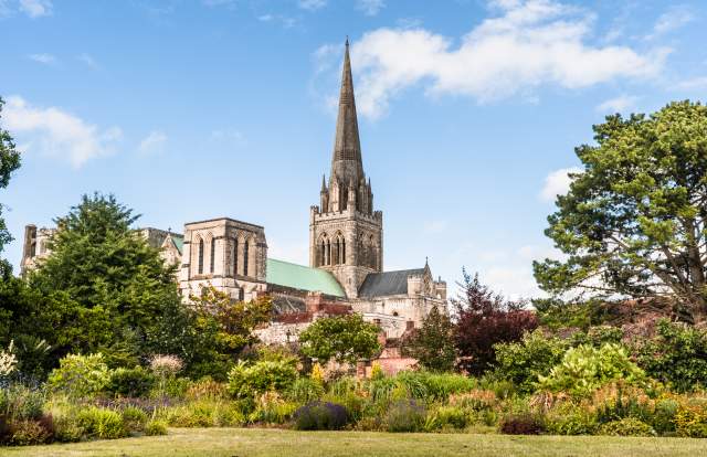 A view of Chichester Cathedral from the gardens with the spire reaching blue sky