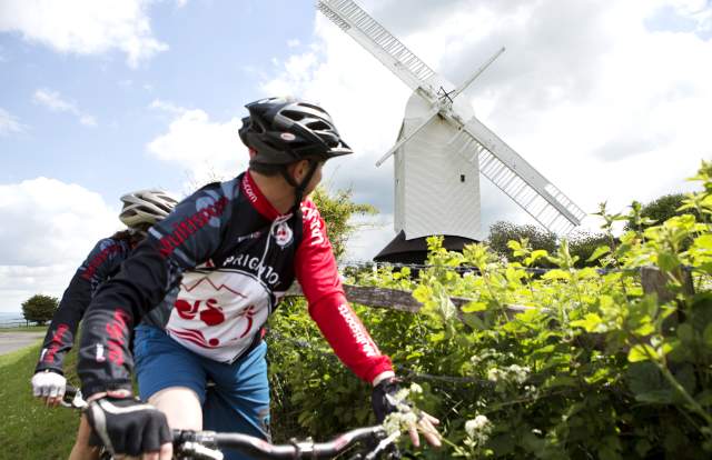 Two mountain bikers ride past a white wooden windmill in the South Downs National Park