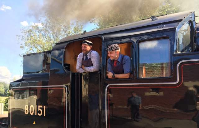 A driver and his crew smiling as they stand in the engine of the Bluebell Railway steam train